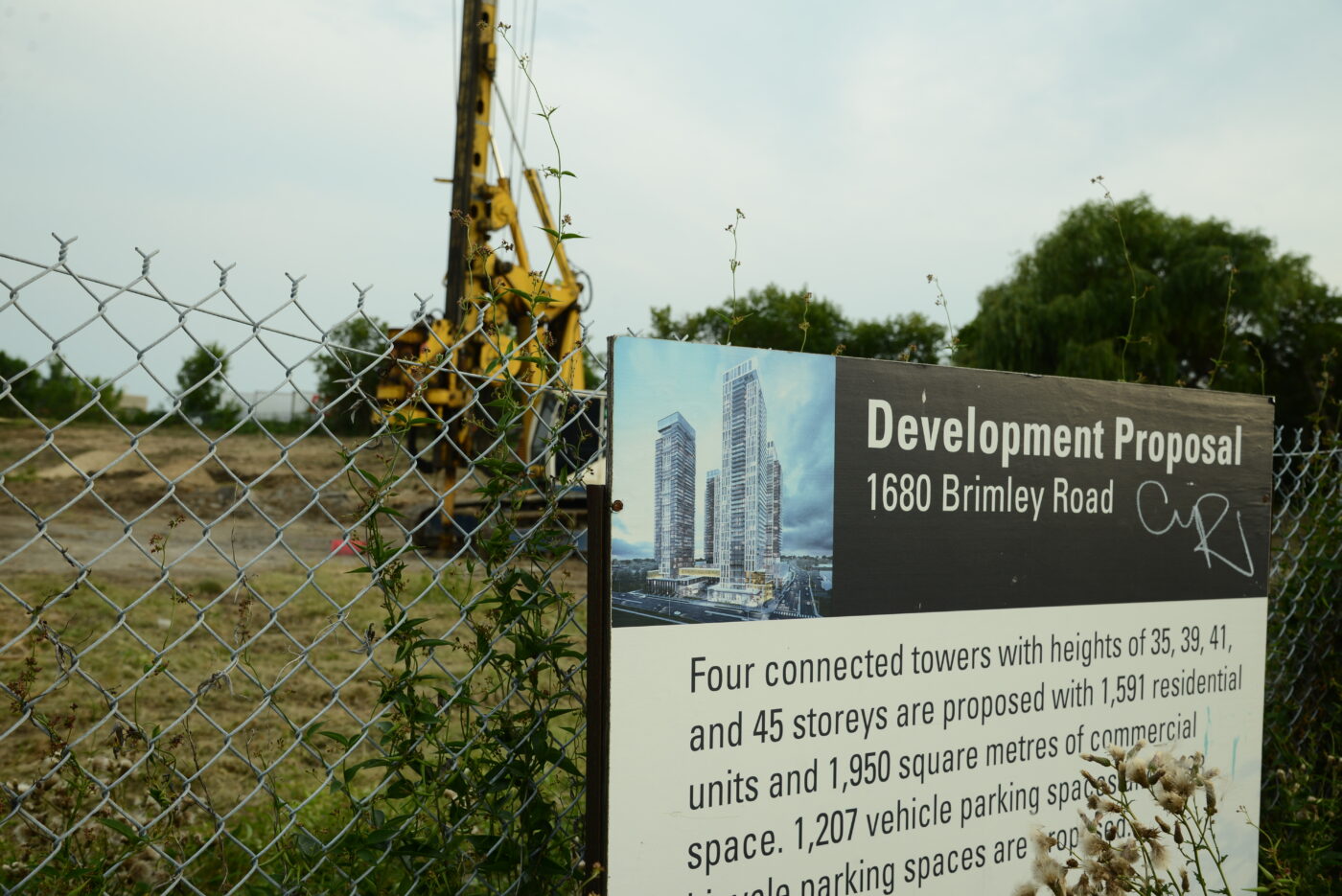 A sign for a proposed residential development is posted on a fence. Behind it, heavy machinery sits unused.