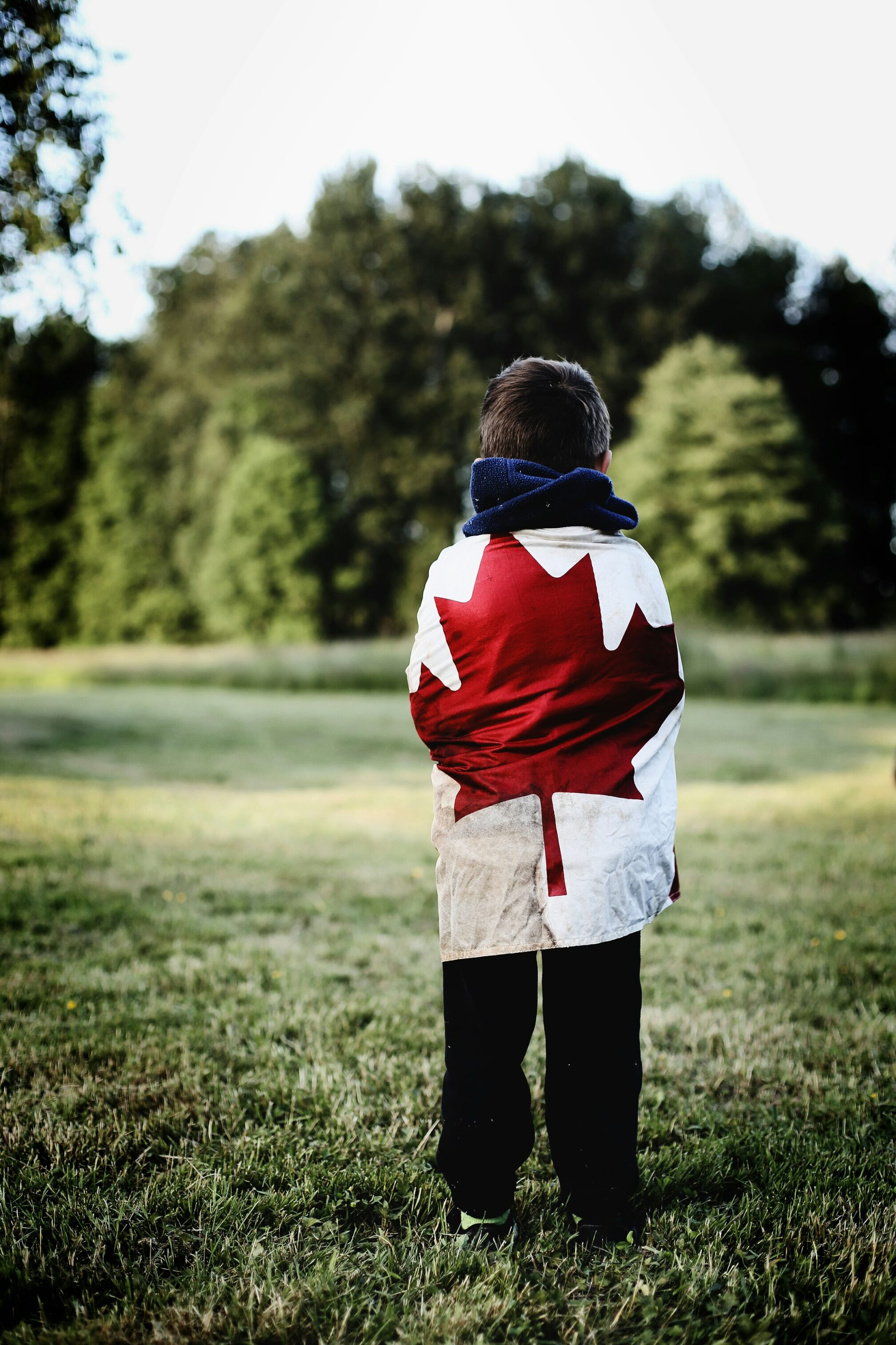 child wearing Canadian flag as a cape on a grassfield