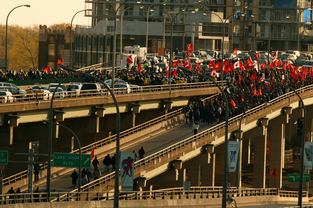 Tamil protesters carrying flags up march up a ramp onto the Gardiner Expressway filling the highway and blocking all traffic in twilight.