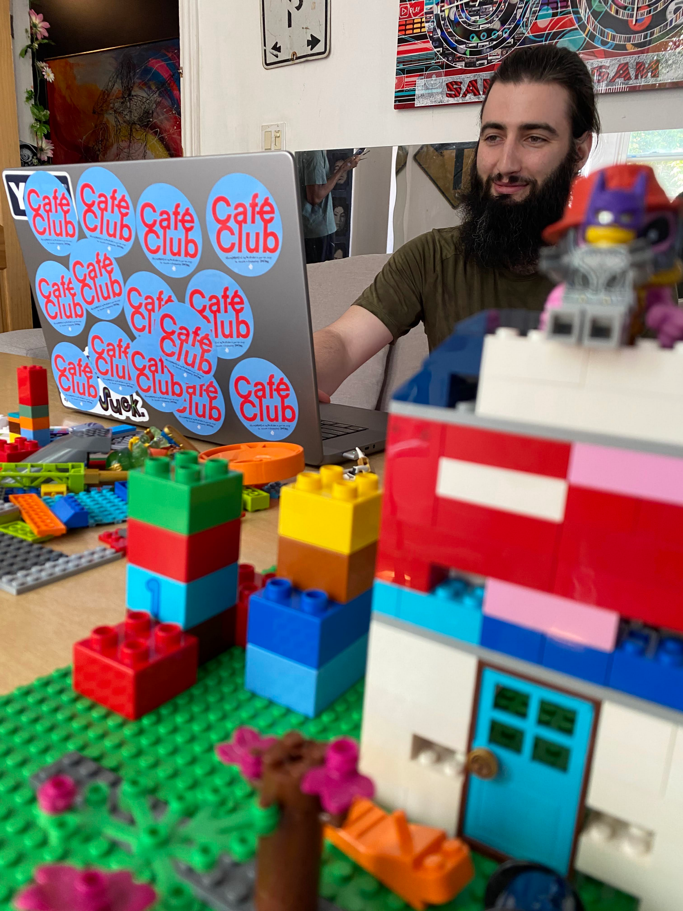 AJ Shoy, Café Club's creator, sits at a table typing on a laptop in the background, as a lego version of the café sits on the table beside him.