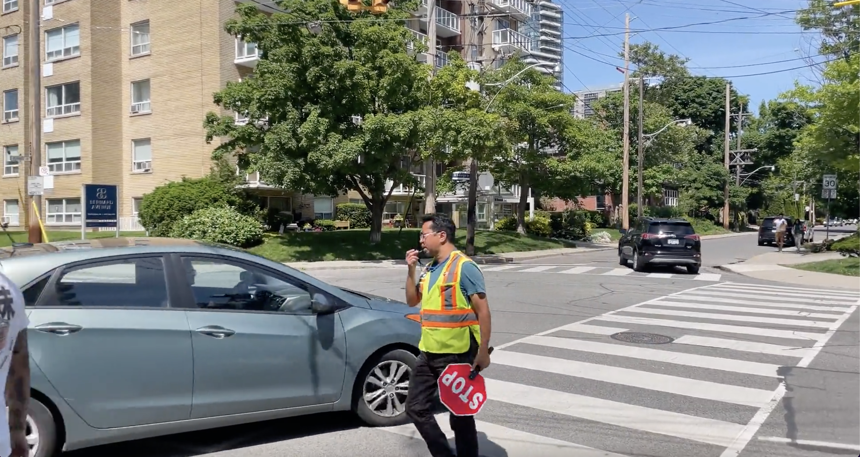 Ulric Singh crosses the street with a stop sign in one hand and a whistle in another.