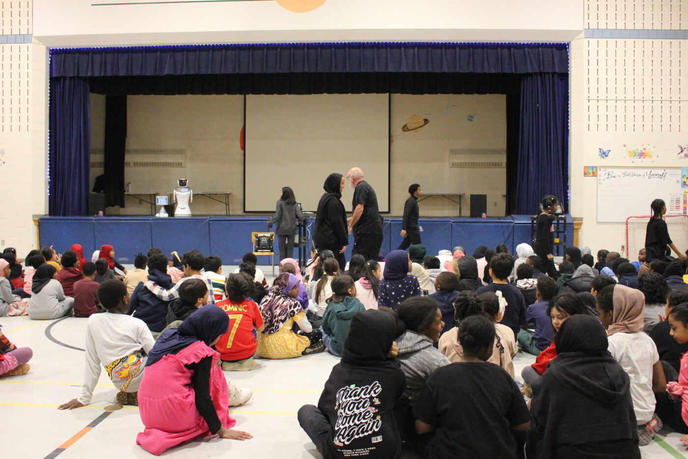 Students at Kingsview Village Jr. Public School sit inside the gymnasium for a presentation by CILAR and GlobalDWS, as part of the Empower to Invent program that's teaching robots and AI to kids.