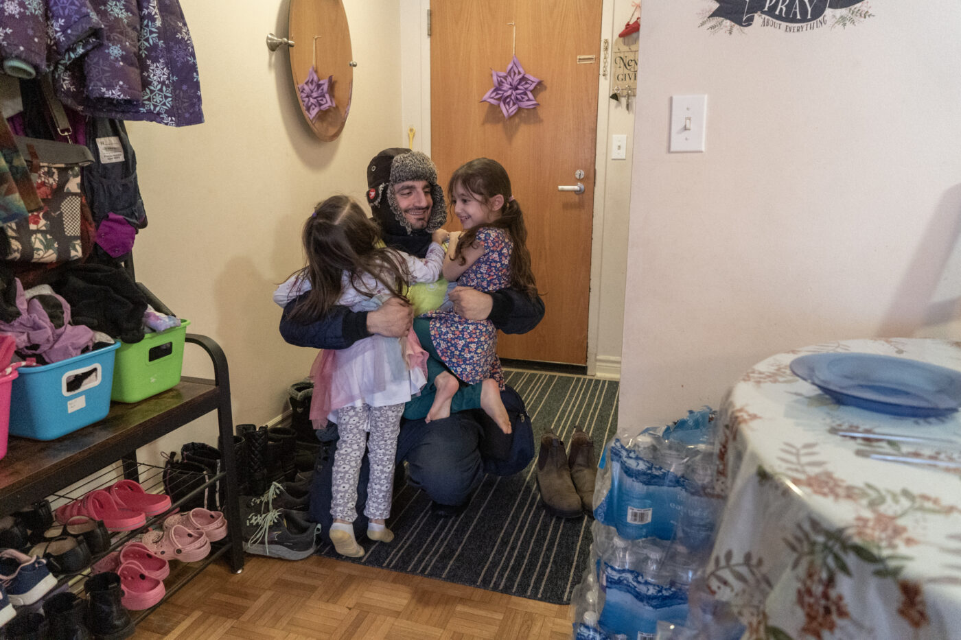 Lilianna and Katalinna (left) excitedly greet thier their father Behnam Eftekhari as he arrives home from work at Canada Post in East York, Canada, on January 17, 2025. Ben Efekhari says "The community dinners really help. Grocery costs have gone up a lot. Sometimes the community dinners have some extra produce or pasta and it helps the rest of the week."