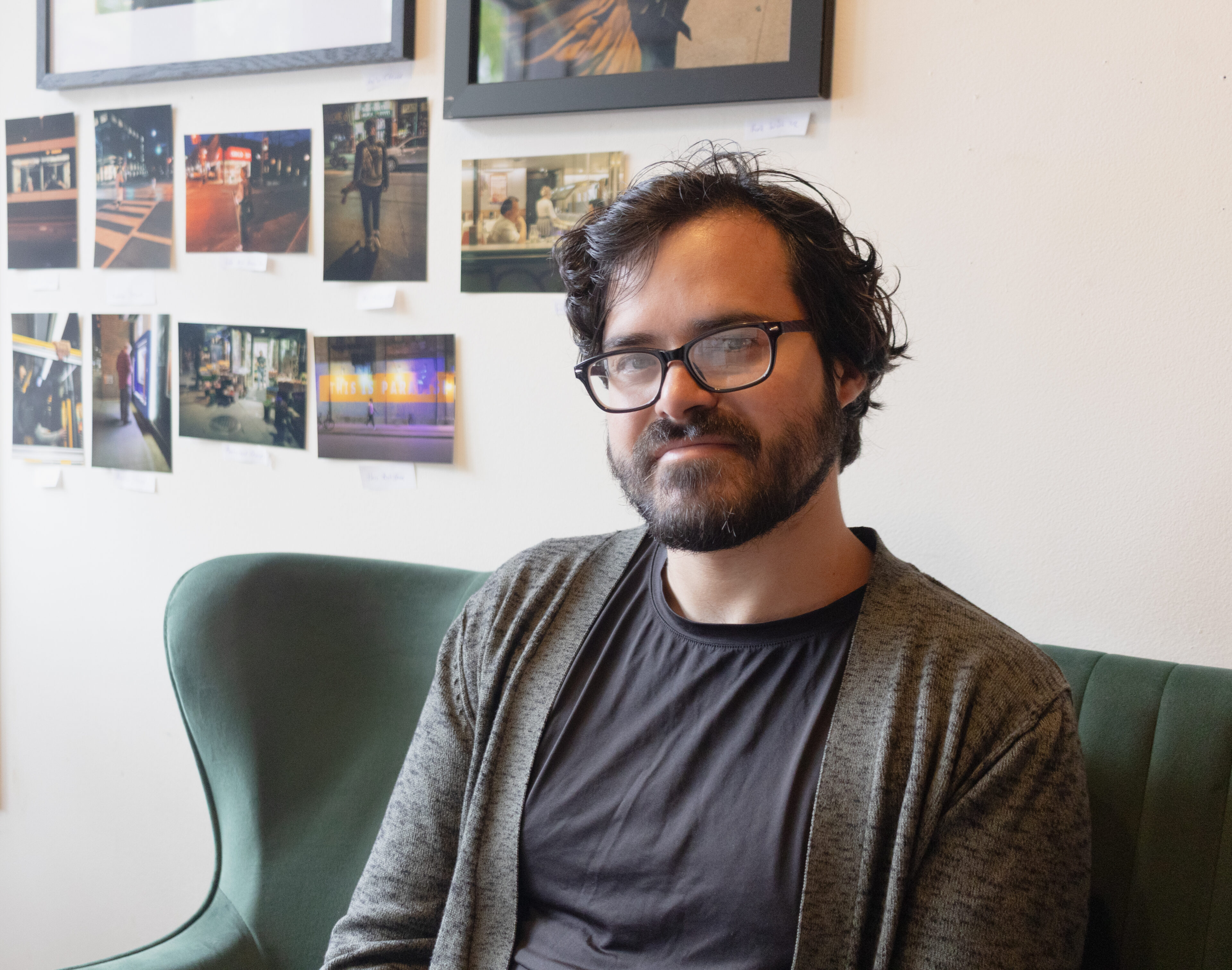 Joshua Zachariah, a man with glasses and a beard sits in a green chair in his bar Danu Social House.