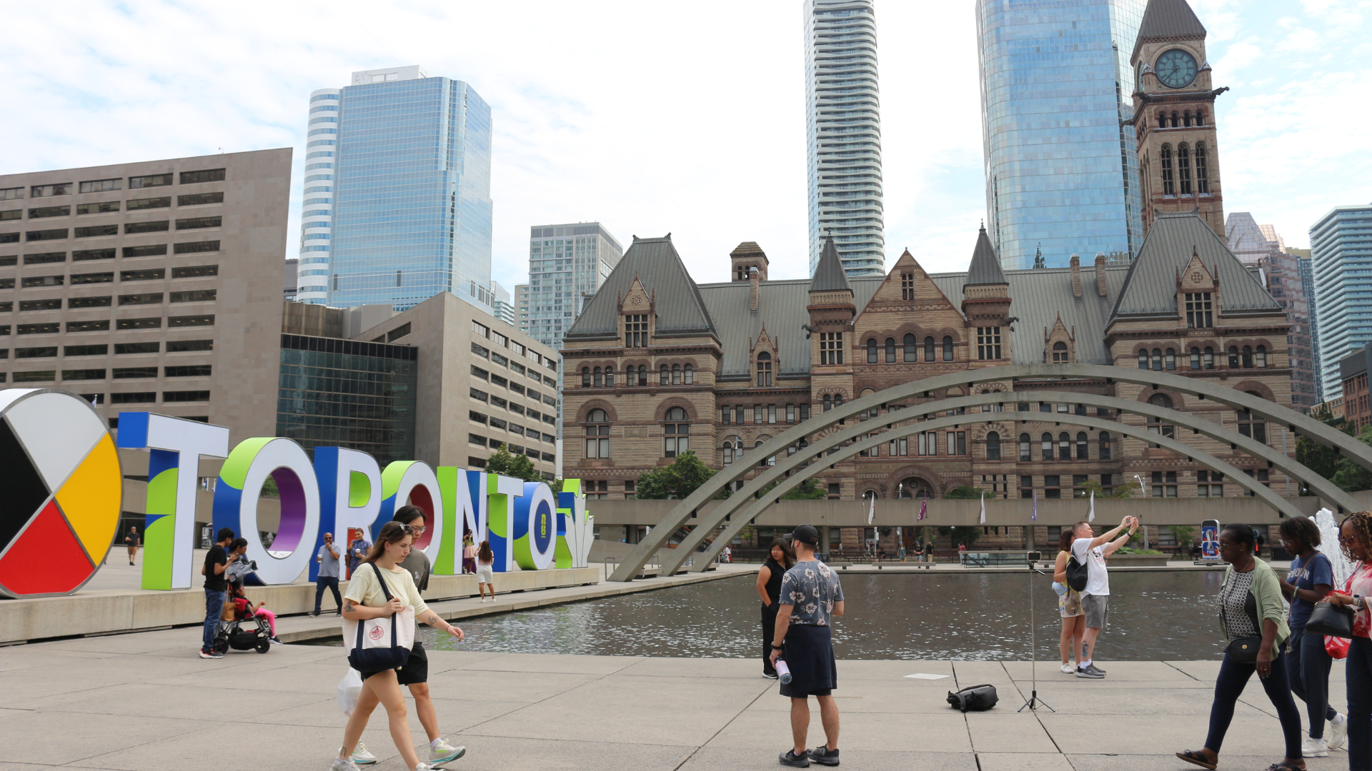 People walk through Nathan Phillips Square in front of the Toronto sign and Toronto City Hall