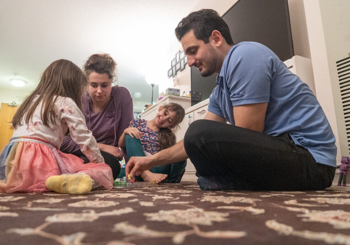 Behnam Eftekhari, wife Juilanna  and daughters Lilianna and Katalinna(left) play a board game in East York, Canada, on January 17, 2025. Ben Efekhari says "The community dinners really help. Grocery costs have gone up a lot. Sometimes the community dinners have some extra produce or pasta and it helps the rest of the week."