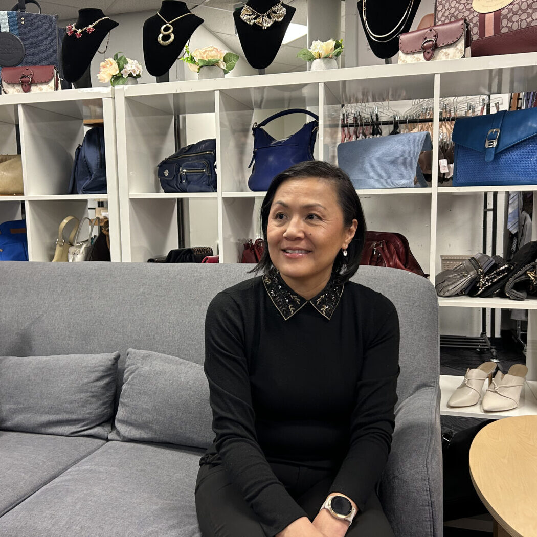 Lichu Chen sitting on a grey couch at the Dress for Success boutique.