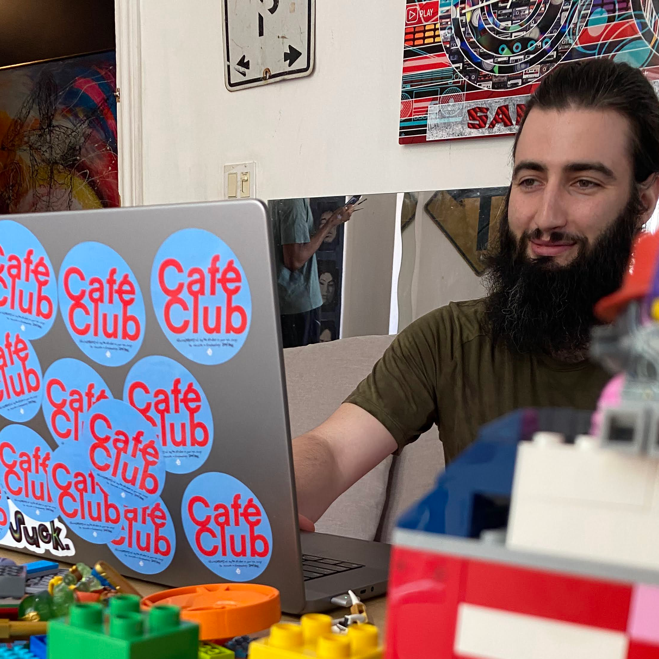 AJ Shoy, Café Club's creator, sits at a table typing on a laptop in the background, as a lego version of the café sits on the table beside him.